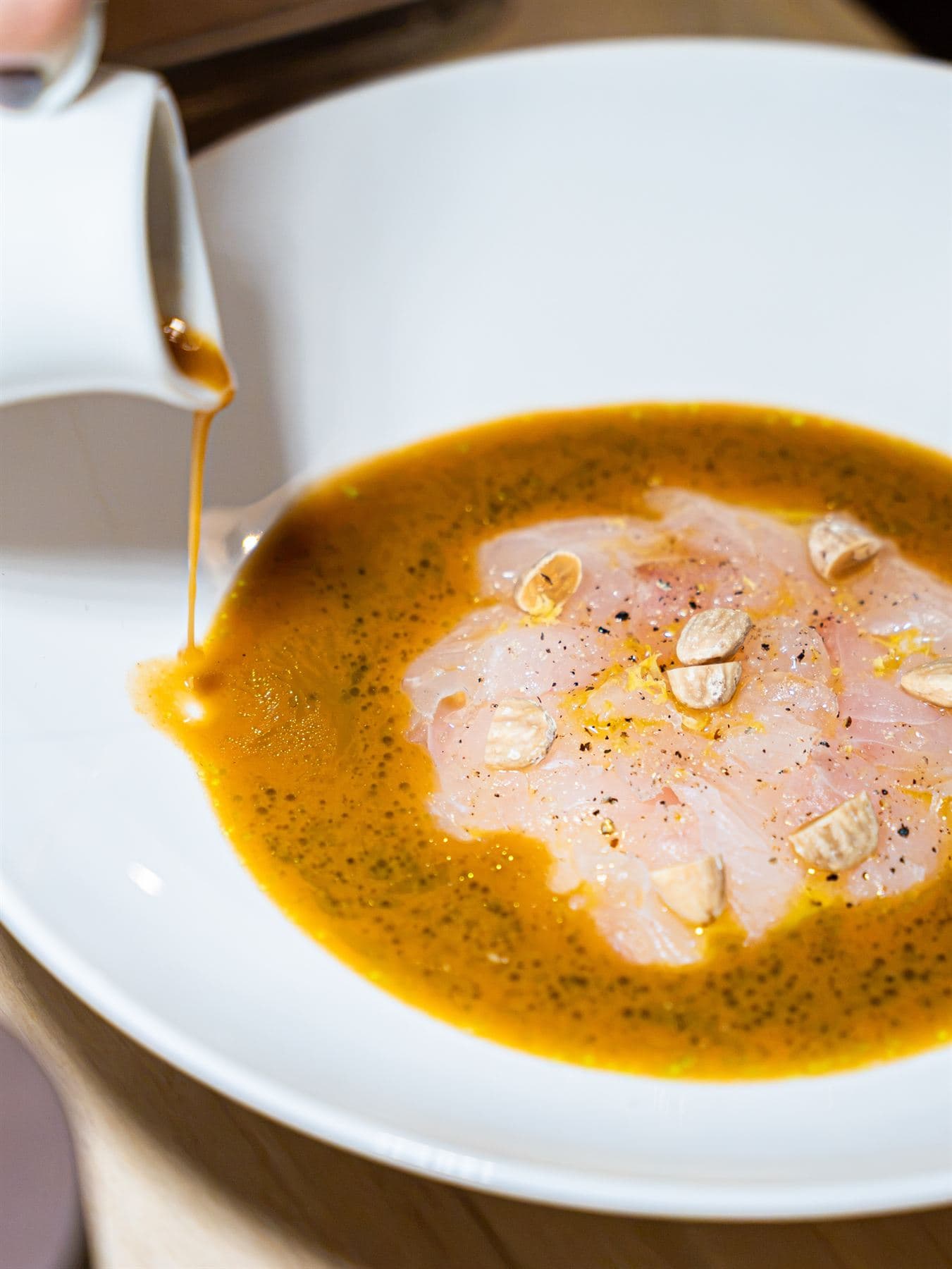 Il fondo agrumato viene versato da una brocchetta sul crudo di pesce già impiattato.